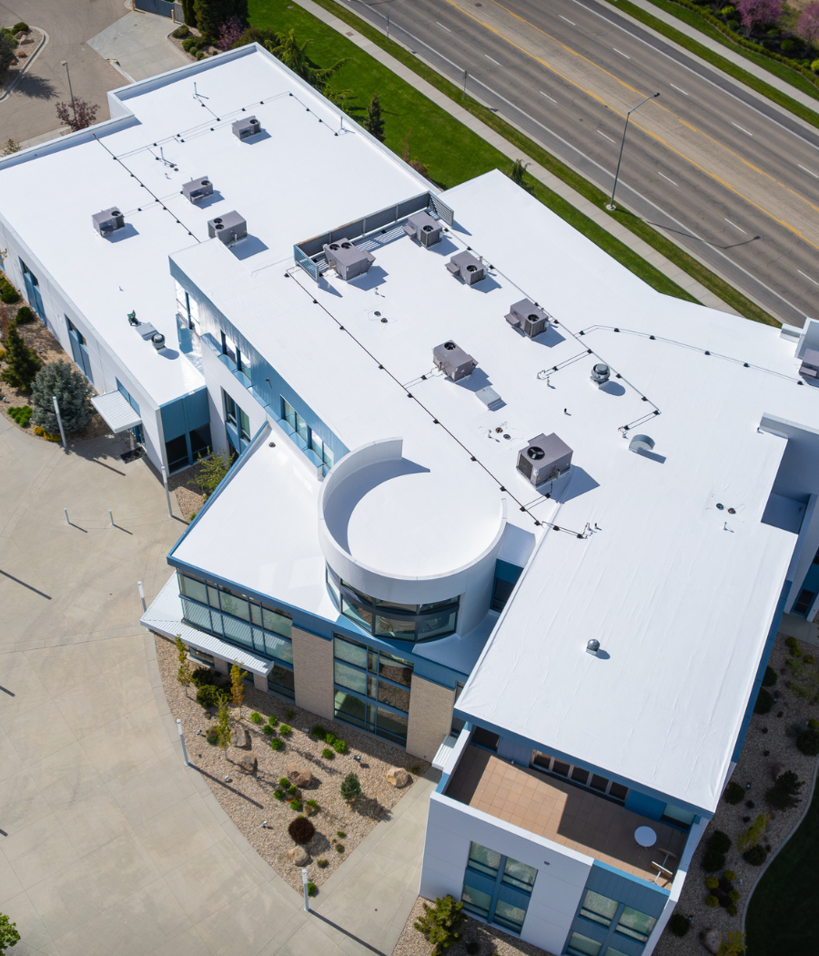Aerial view of a modern commercial building with a clean white flat roofing system and multiple rooftop HVAC units.