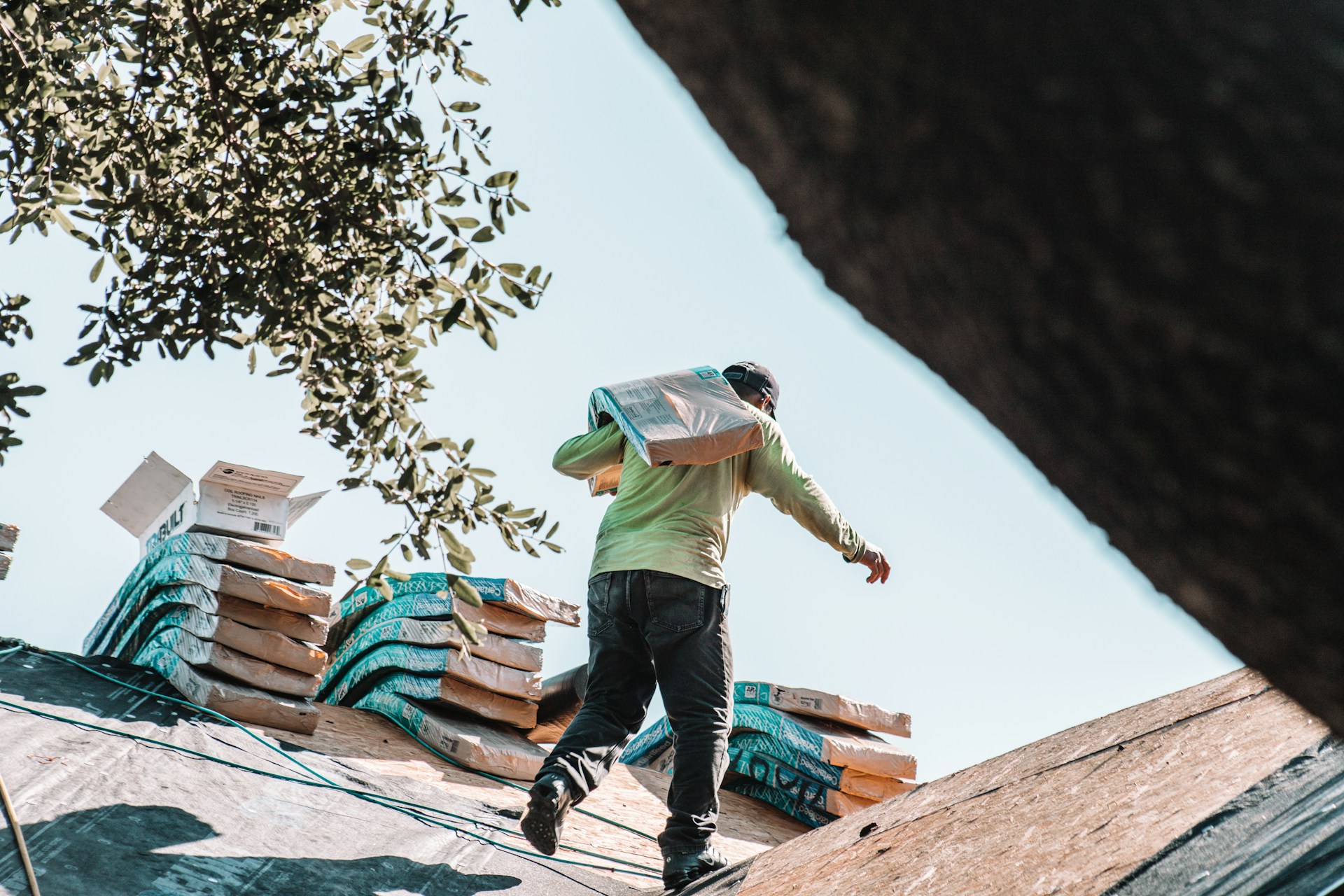 man carrying 3-tab roof shingles up a slope