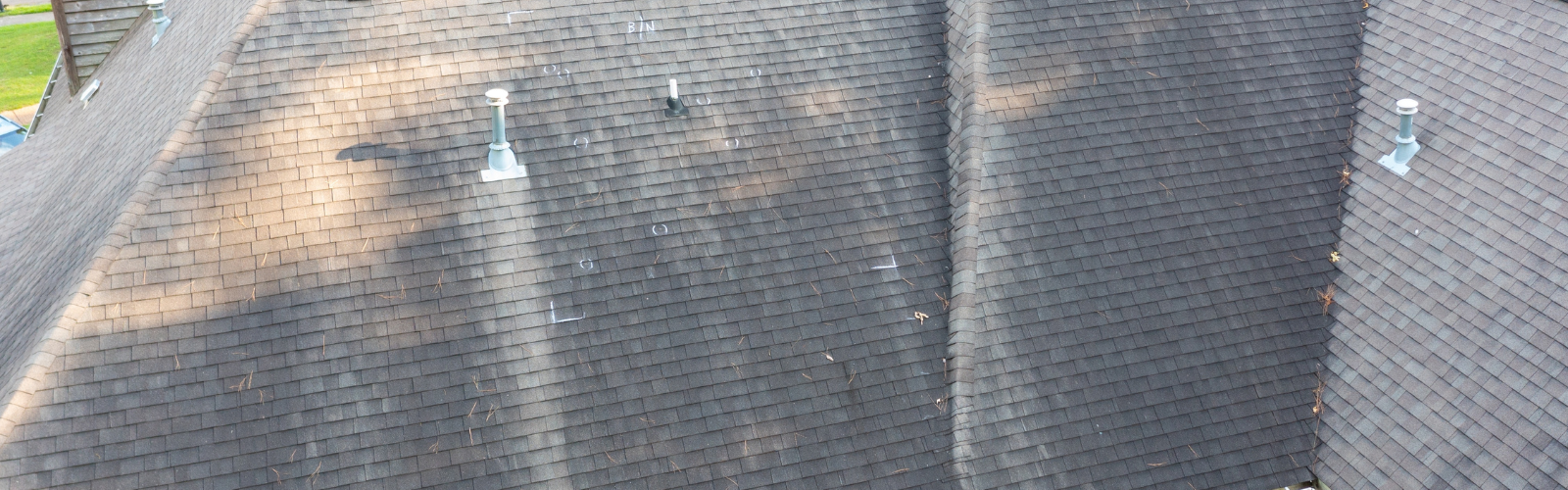 Aerial view of a residential shingle roof showing hail impact marks, wind-blown shingle misalignment, and debris accumulation.