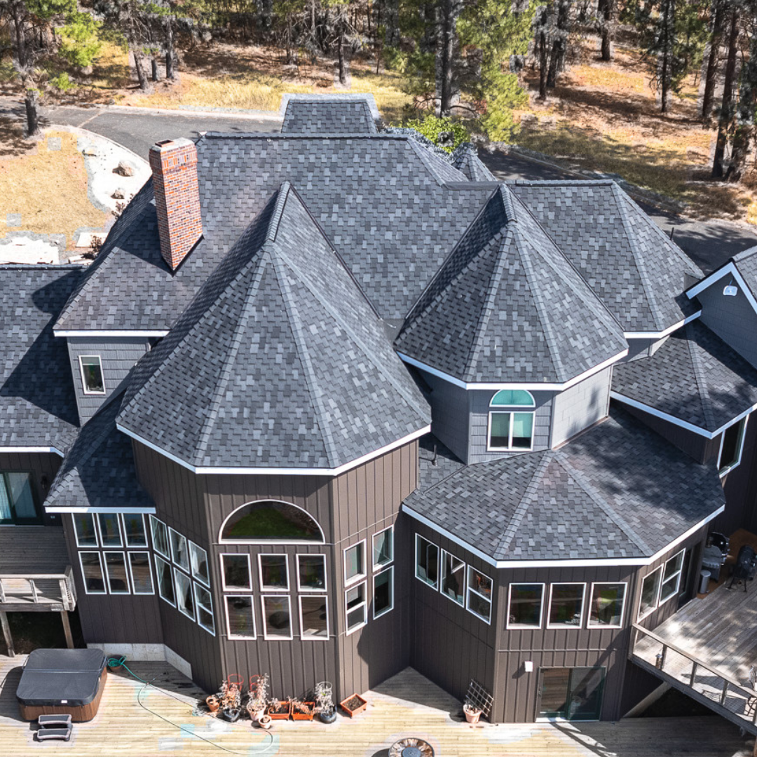 Large custom home with complex multi-angled roofing covered in dark Presidential-style shingles.