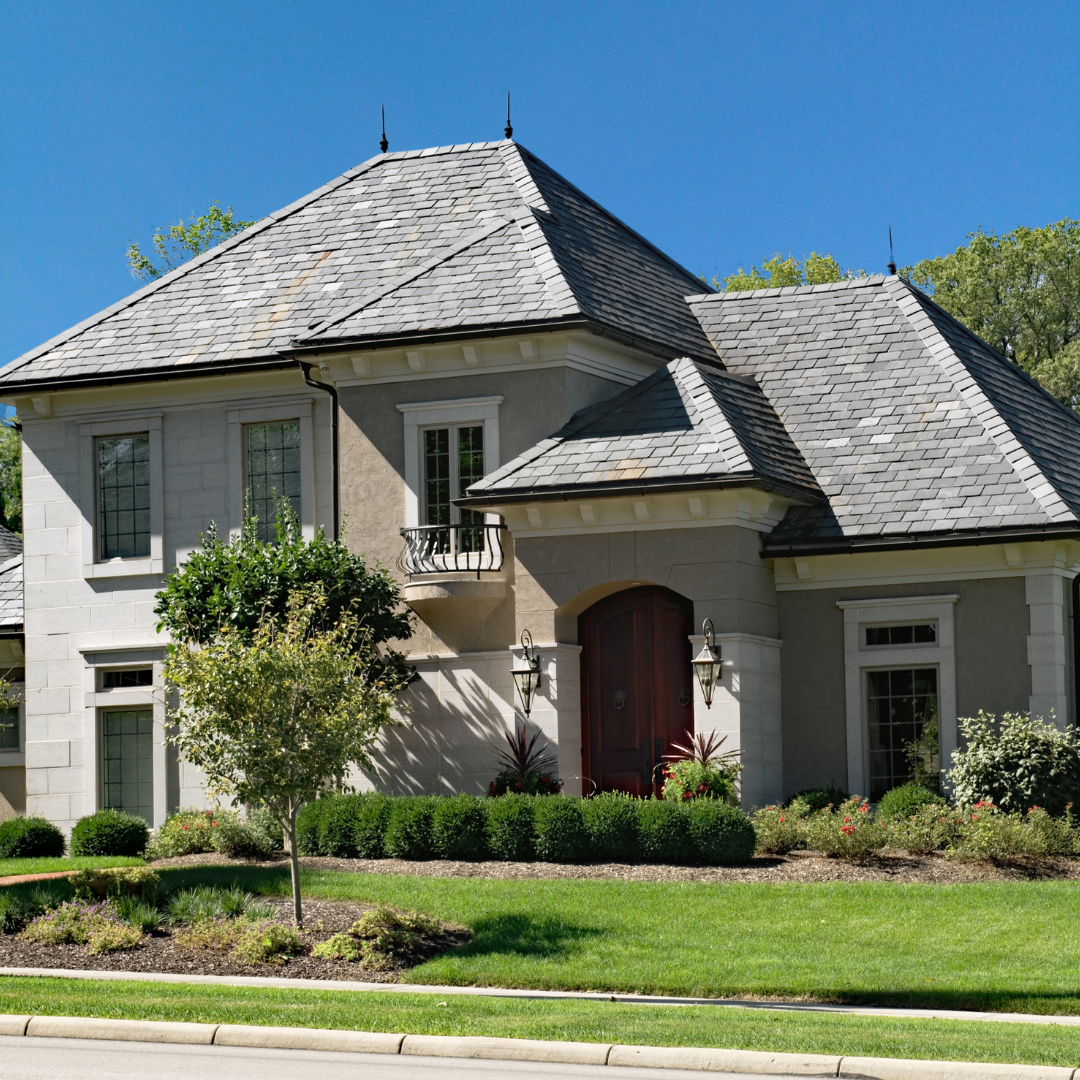 Elegant home with gray slate roofing, stucco and stone exterior, and well-manicured landscaping.