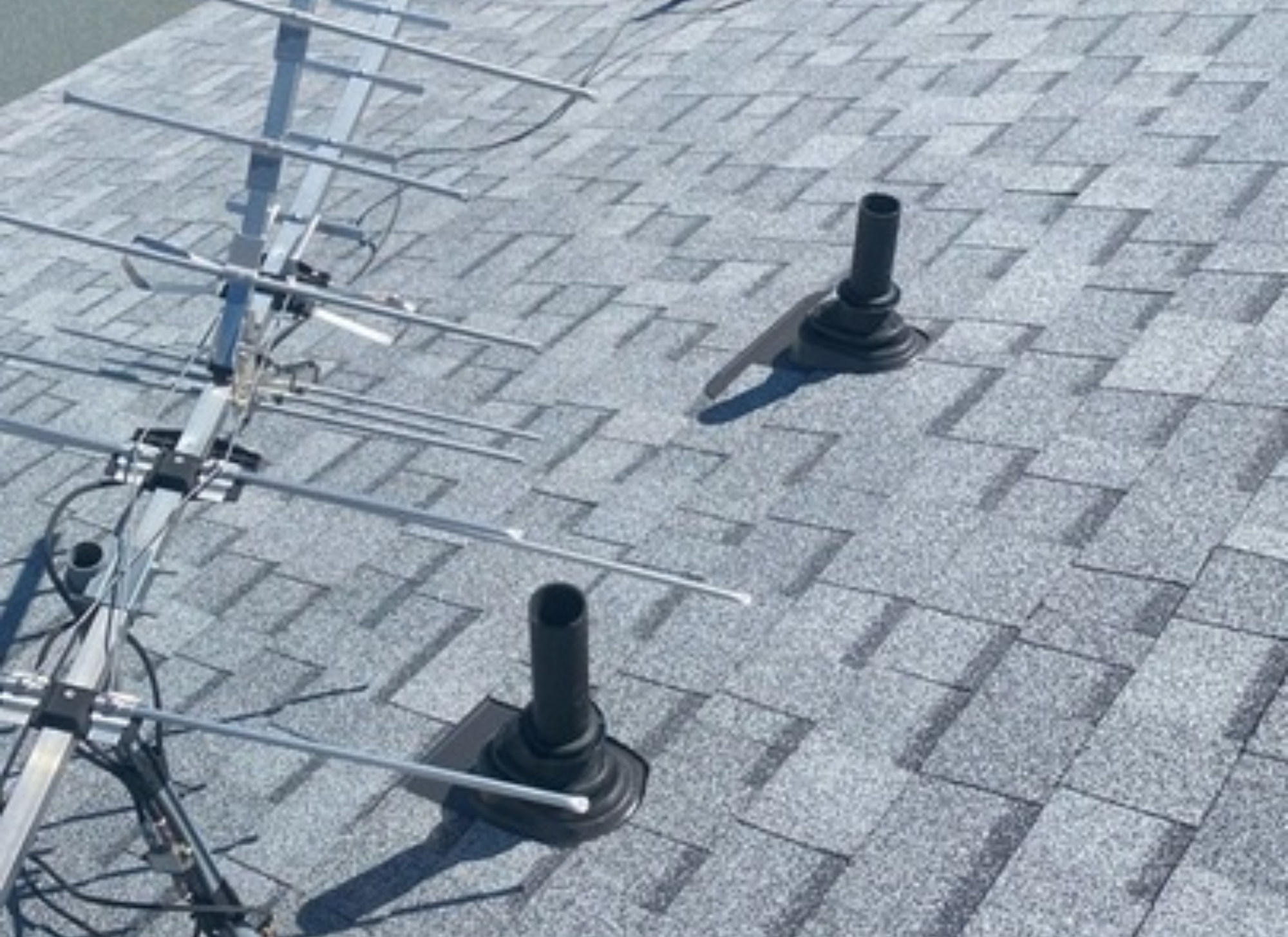 Asphalt shingle roof with two black lifetime pipe boots installed around vent pipes, next to a rooftop antenna system.