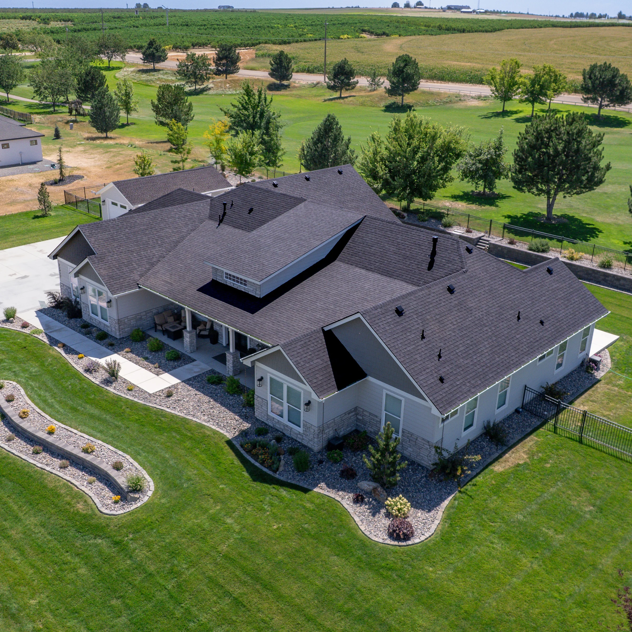 Aerial view of a large residential home featuring a new black asphalt shingle roof and landscaped yard.