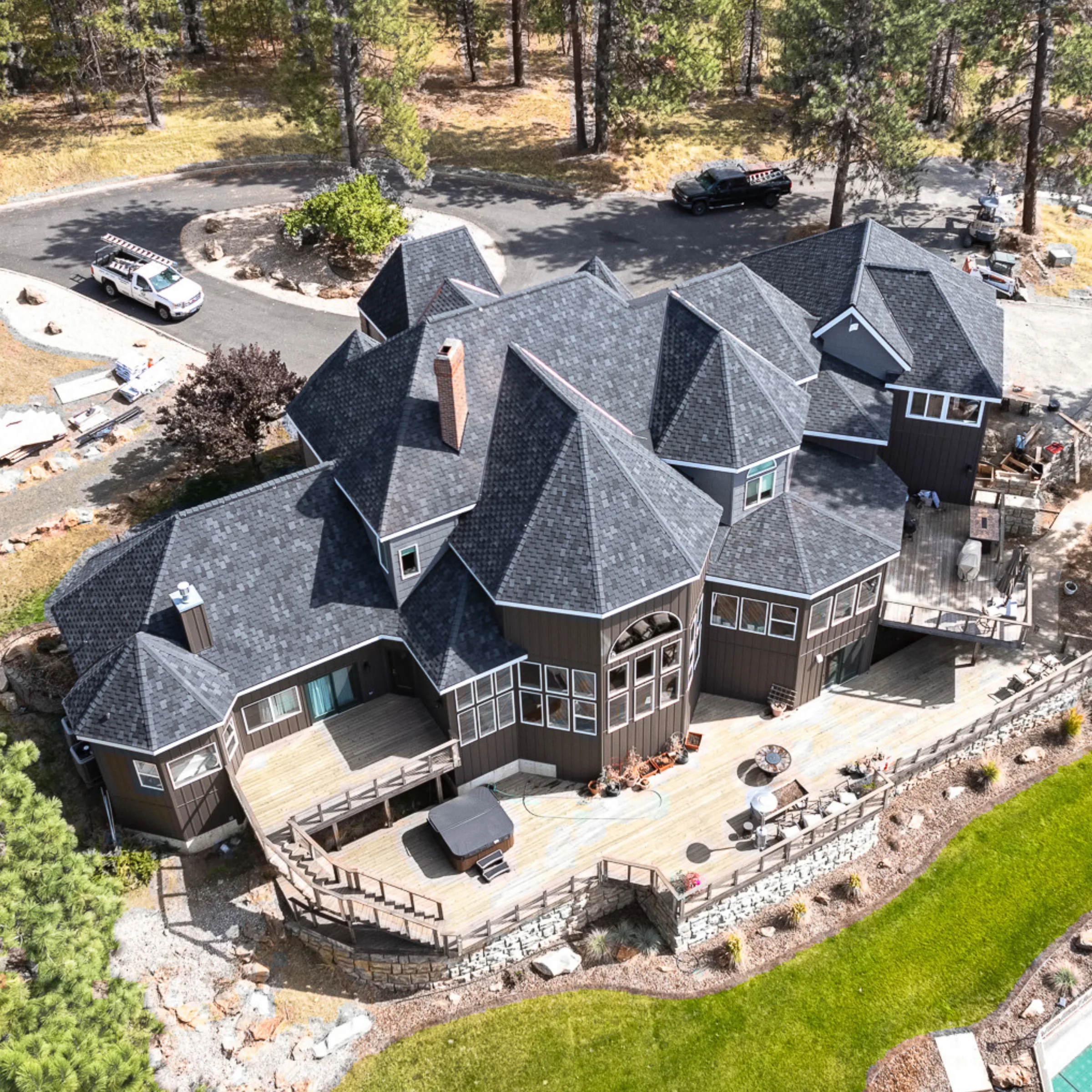 Overhead photo of a large luxury home with multiple roof sections and dark asphalt shingles, surrounded by trees.