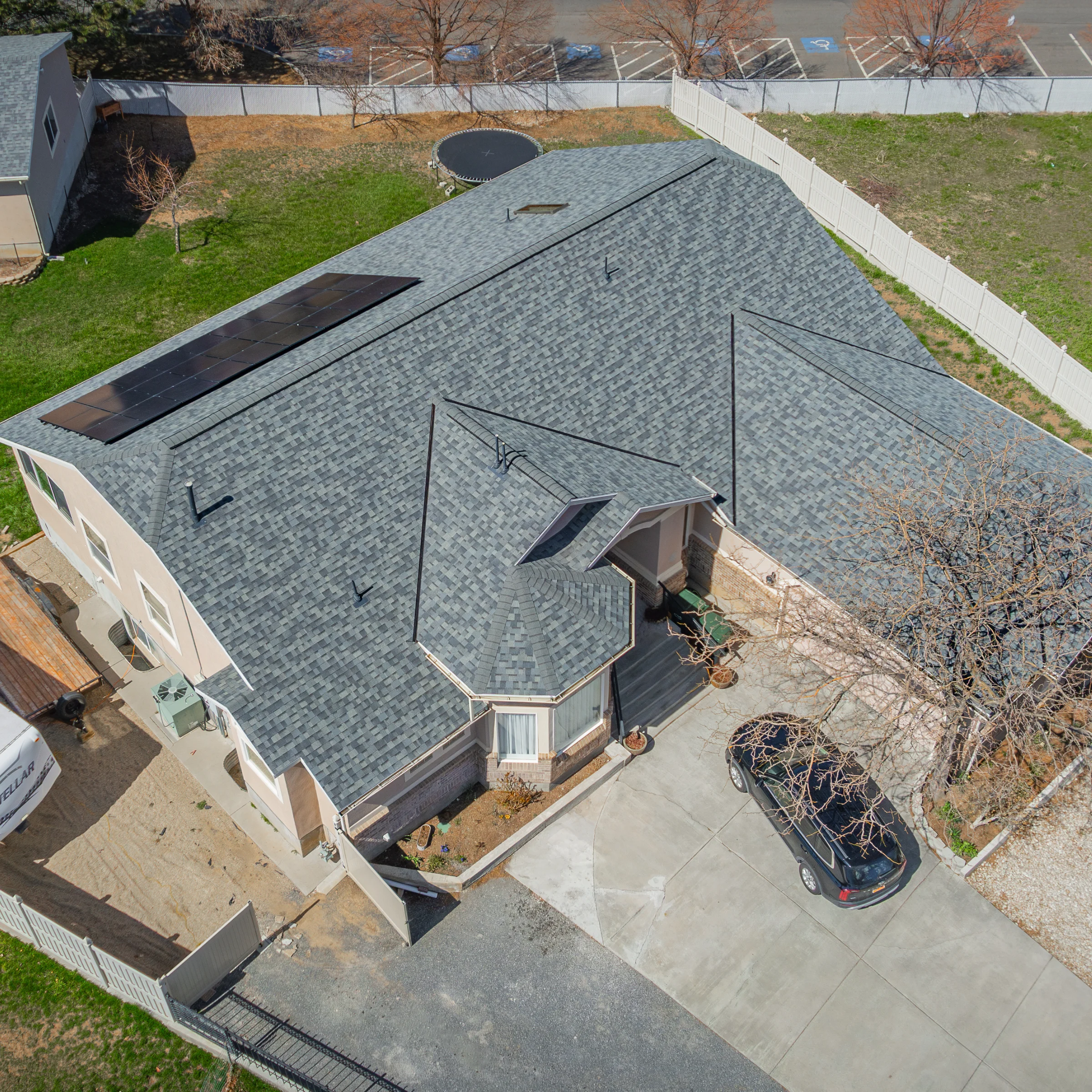 Aerial view of a residential home with gray asphalt shingles and solar panels installed on the roof.