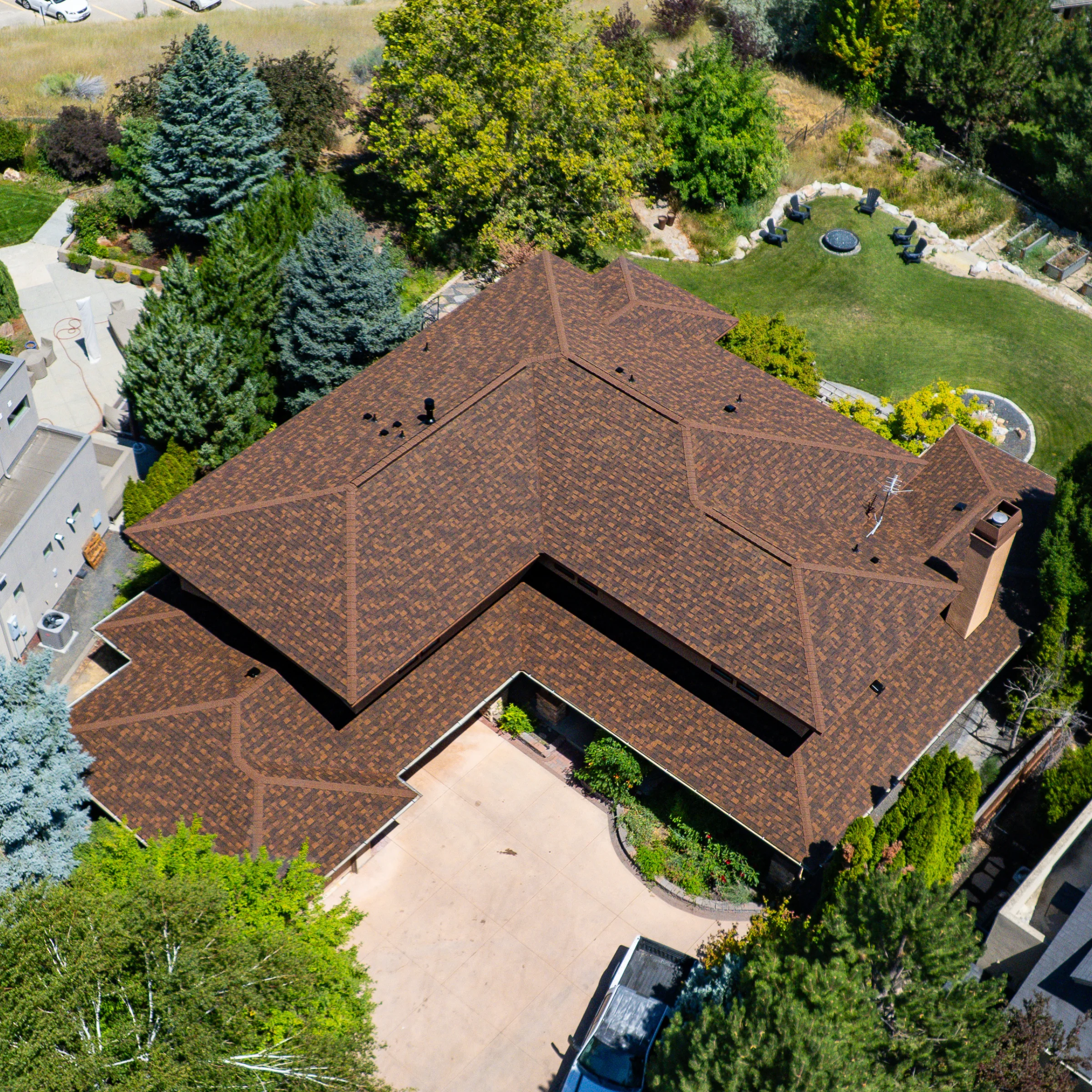 Overhead shot of a suburban home with a new brown asphalt shingle roof and landscaped backyard.