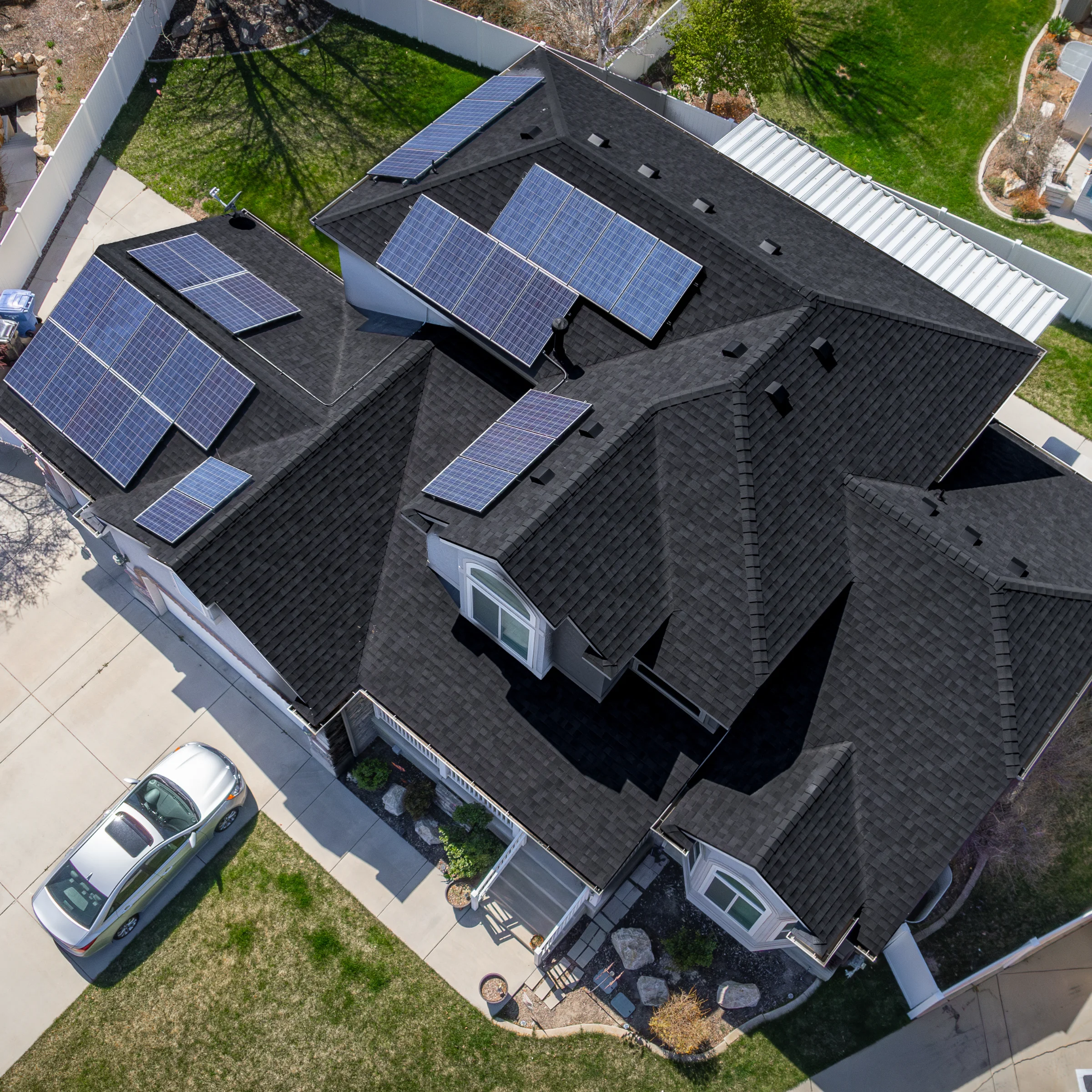Aerial view of a modern home with black asphalt shingles and multiple solar panels across the roof.